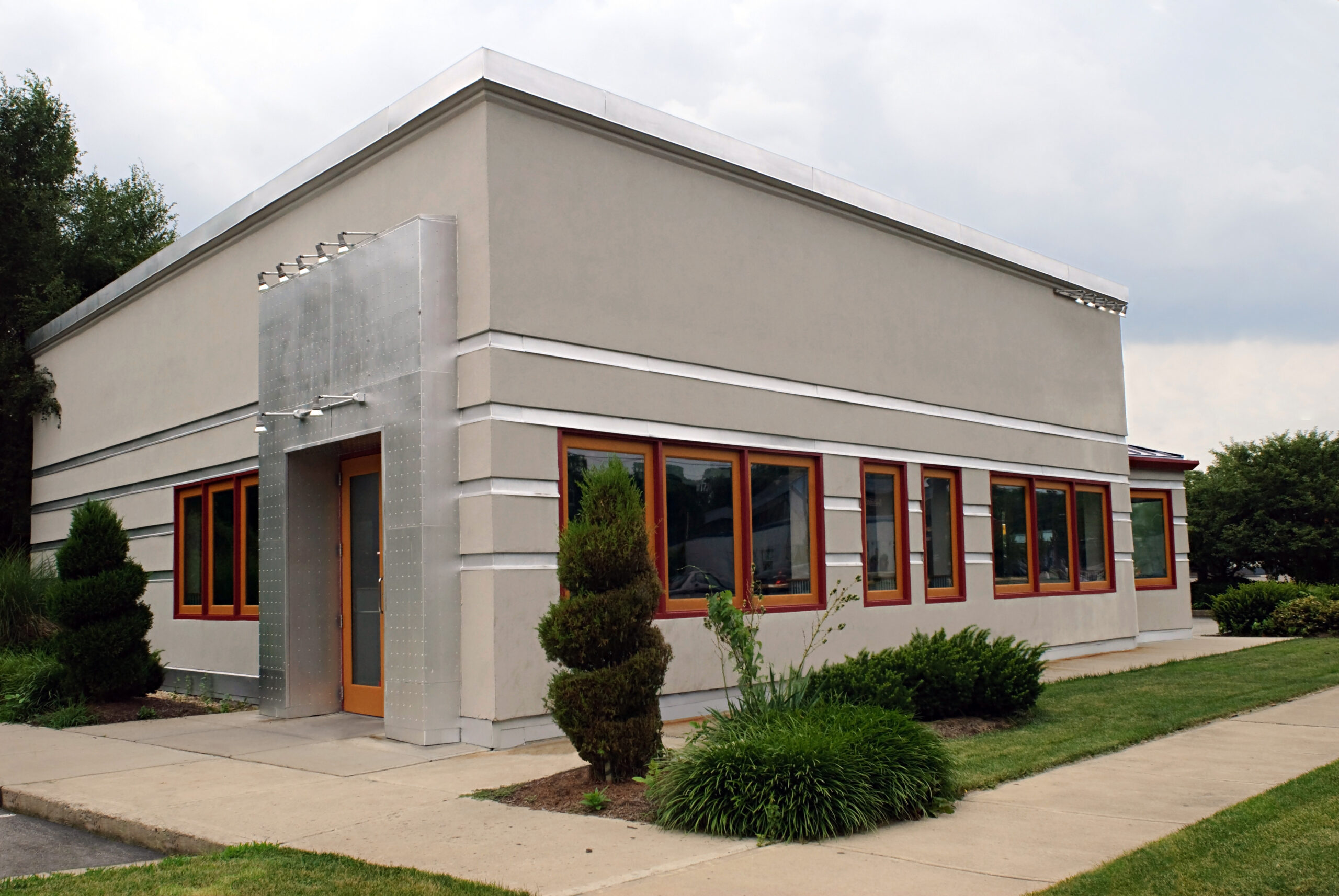 A restaurant building on the corner with gray stucco and a metal modern entrance.