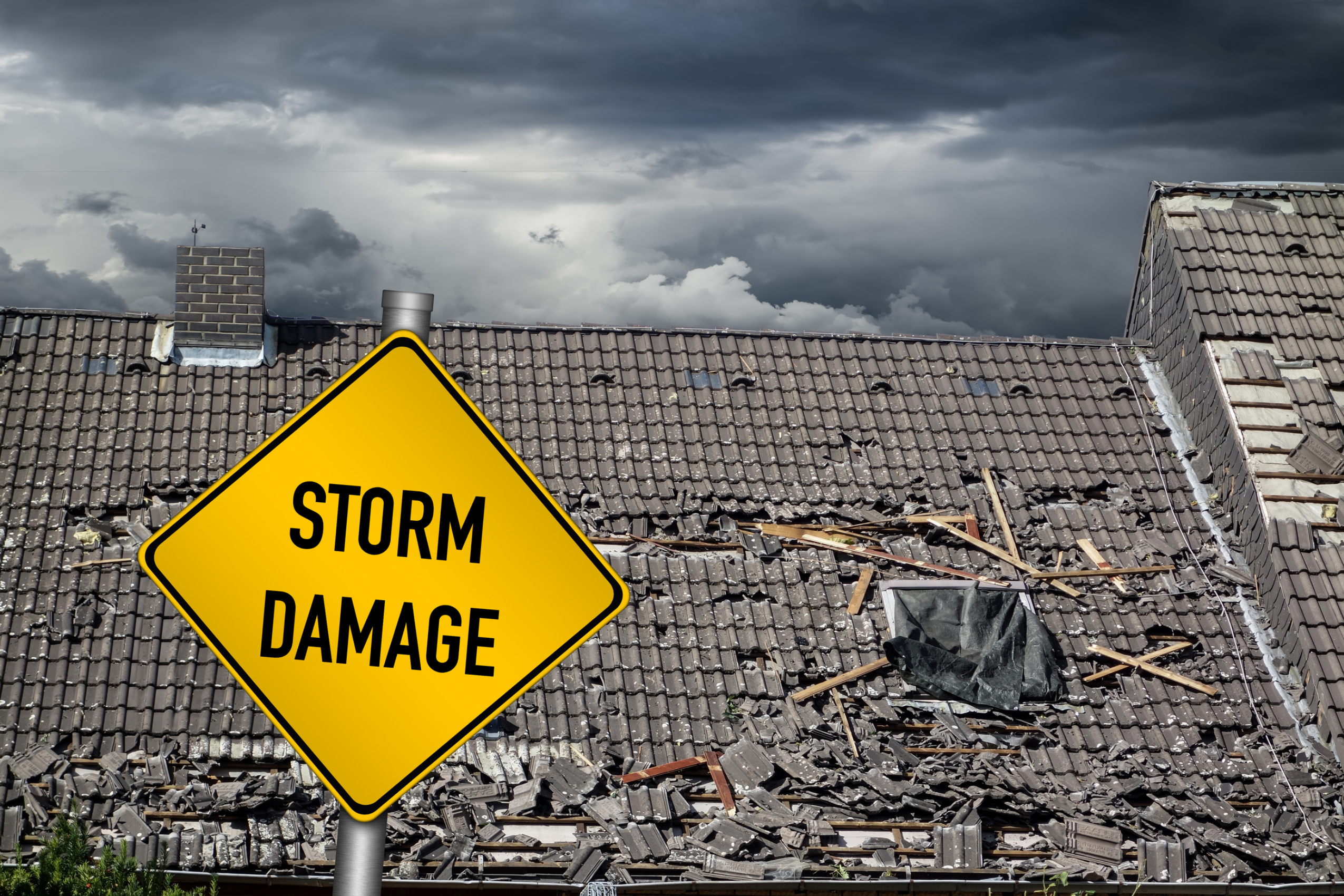 Very damaged rooftop with a stormy dark sky behind it visible and a yellow sign with black bold text: STORM DAMAGE